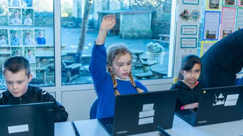 Pupils in an IT lesson, a girl holds up her hand to answer a question